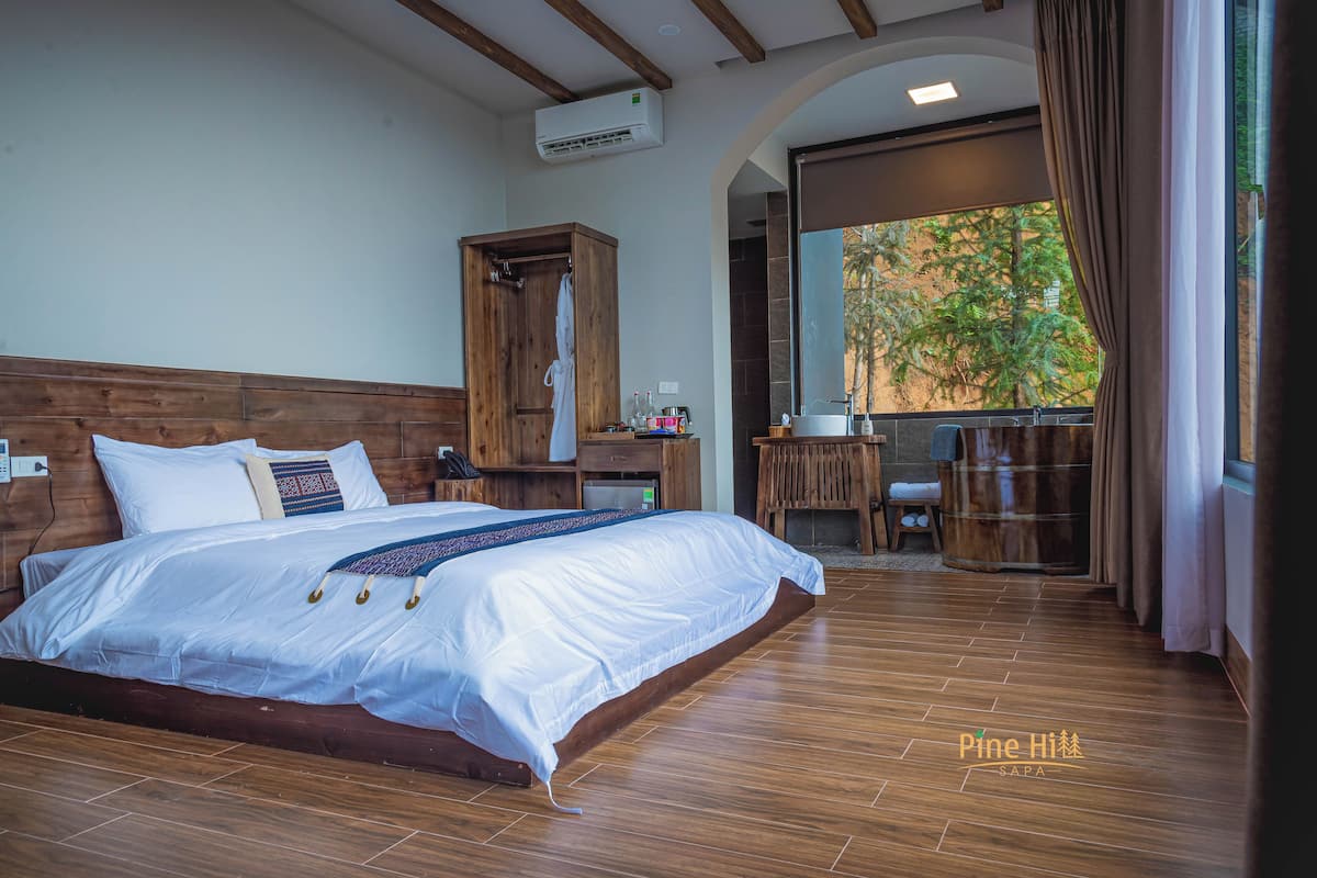 Ein geräumiges Schlafzimmer mit einem großen Bett, einem Holzkopfstück und Blick ins Freie durch ein Fenster.