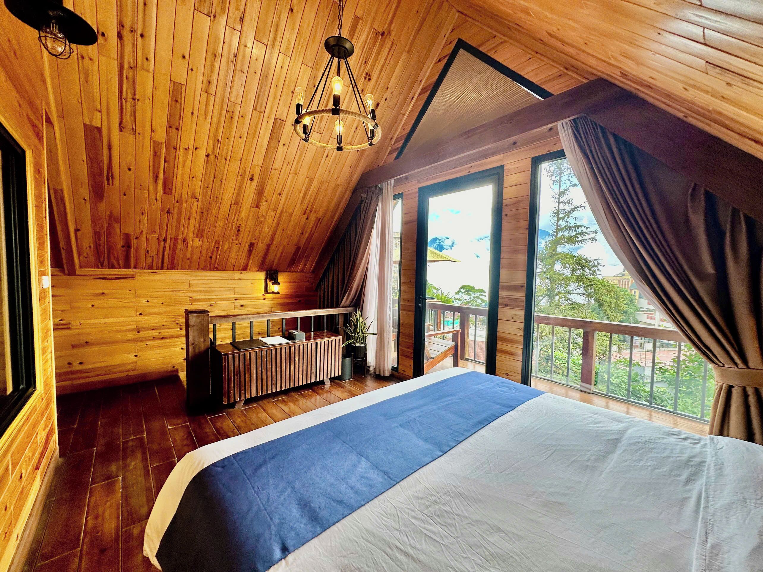 A wooden cabin bedroom with a large bed, a wooden desk, and a balcony with a view.