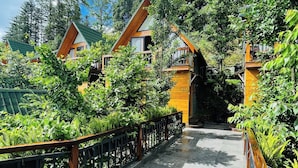 Un sentier mène à une rangée de cabanes aux toits en bois, entourées d’une végétation luxuriante.