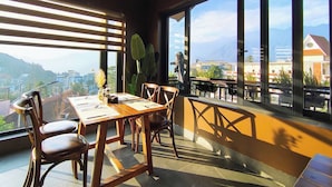 Un coin repas avec une table et des chaises en bois, de grandes fenêtres offrant une vue sur les montagnes et un balcon avec des sièges d’extérieur.