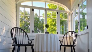 A sunroom with two chairs, a table, and large windows offering a view of trees.