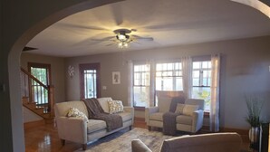 A living room with a sofa, armchairs, a rug, and a ceiling fan.