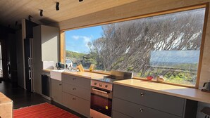 A modern kitchen with a large window, stainless steel appliances, and a red rug. - Welcome to Admiral Cabin, a luxurious off-grid retreat on King Island, Tasmania. (Nugara)
