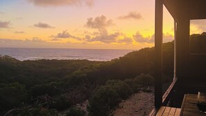 A beach view from a wooden deck with a view of the ocean and a sunset. - Welcome to Admiral Cabin, a luxurious off-grid retreat on King Island, Tasmania. (Nugara)