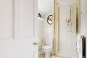 Une salle de bain avec des toilettes blanches, une douche dotée d’un cadre doré et un miroir également doté d’un cadre doré.