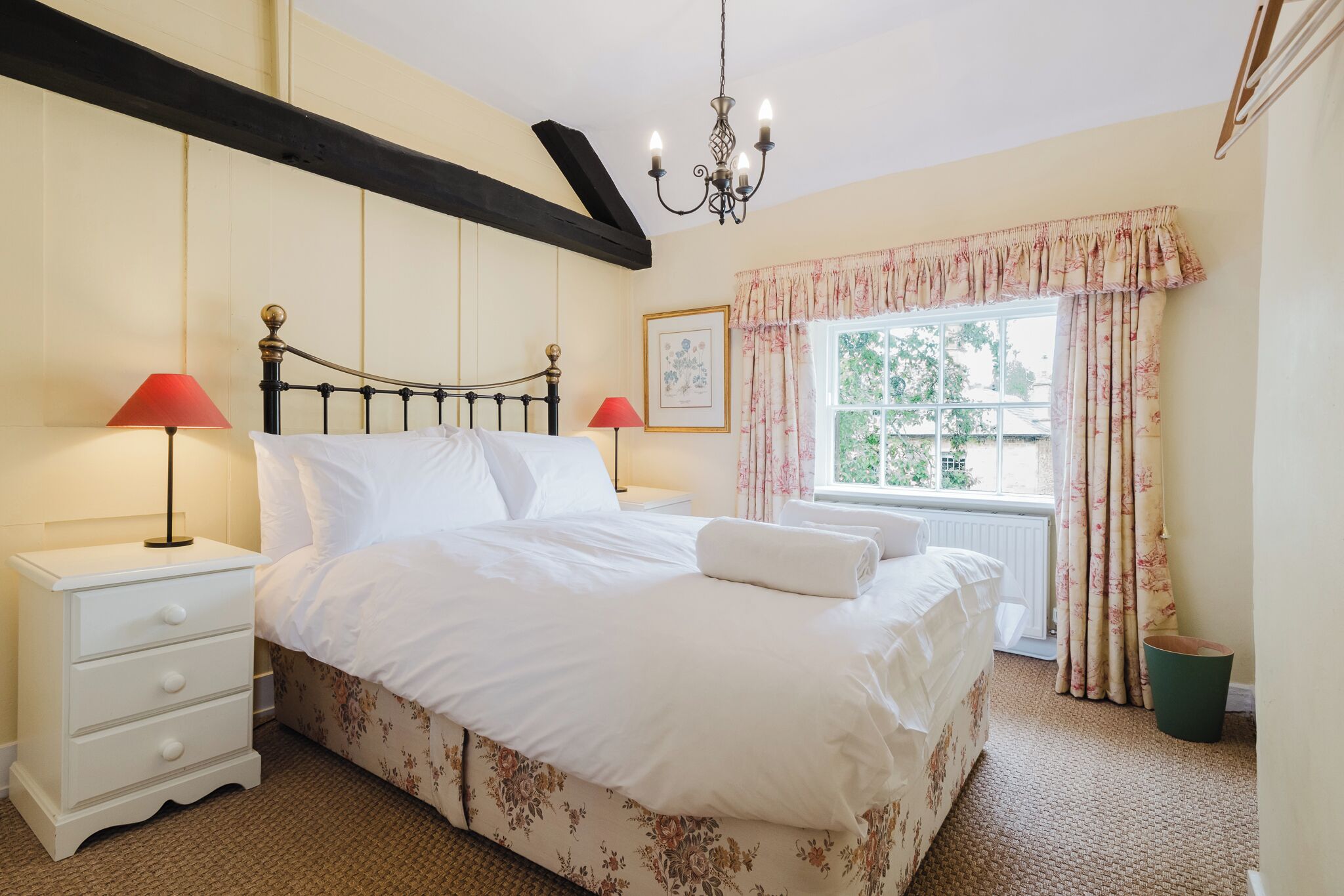 A bedroom with a bed, nightstands, a window with curtains, a chandelier, and a radiator.