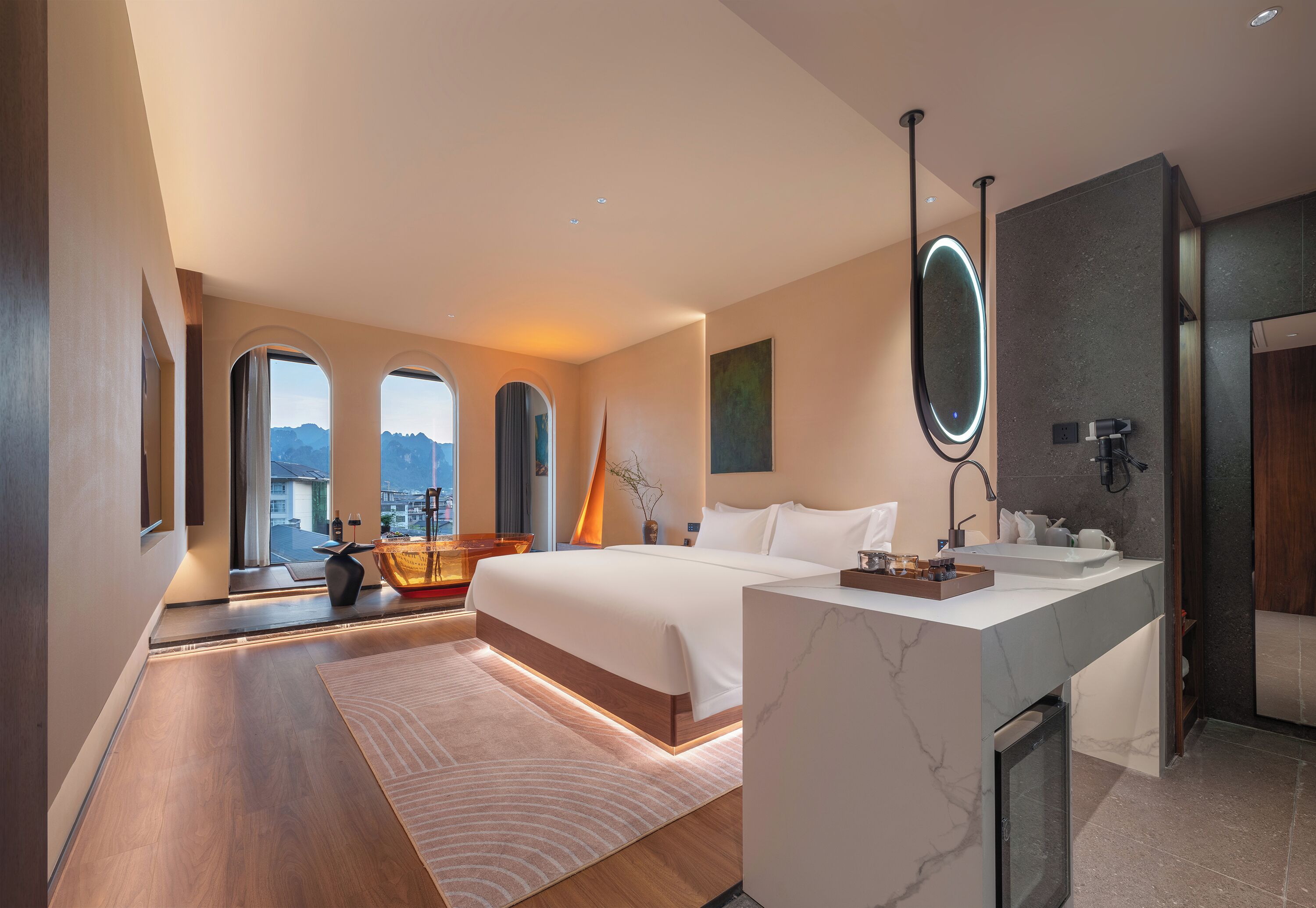 A modern hotel room with a large bed, a bathroom with a marble vanity, and a city view through the windows.