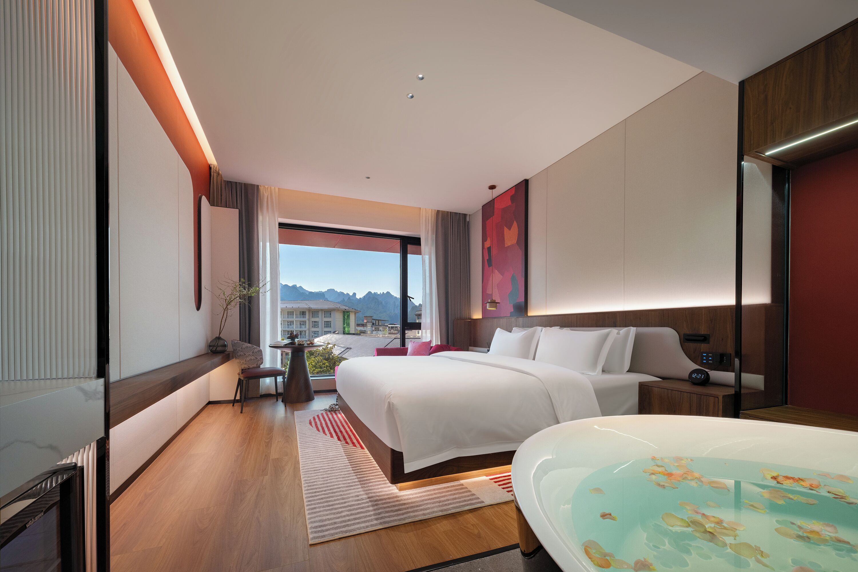 Une chambre d’hôtel moderne dotée d’un grand lit, d’un coin salon, d’une baignoire et offrant une vue sur les montagnes.