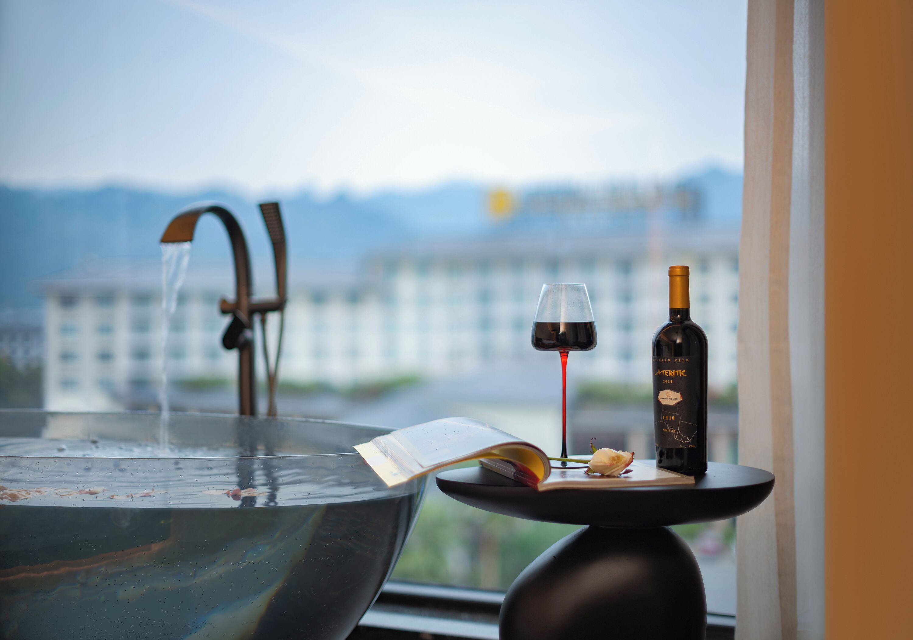 A window view with a large bowl, a wine bottle, and a glass of wine on a table.