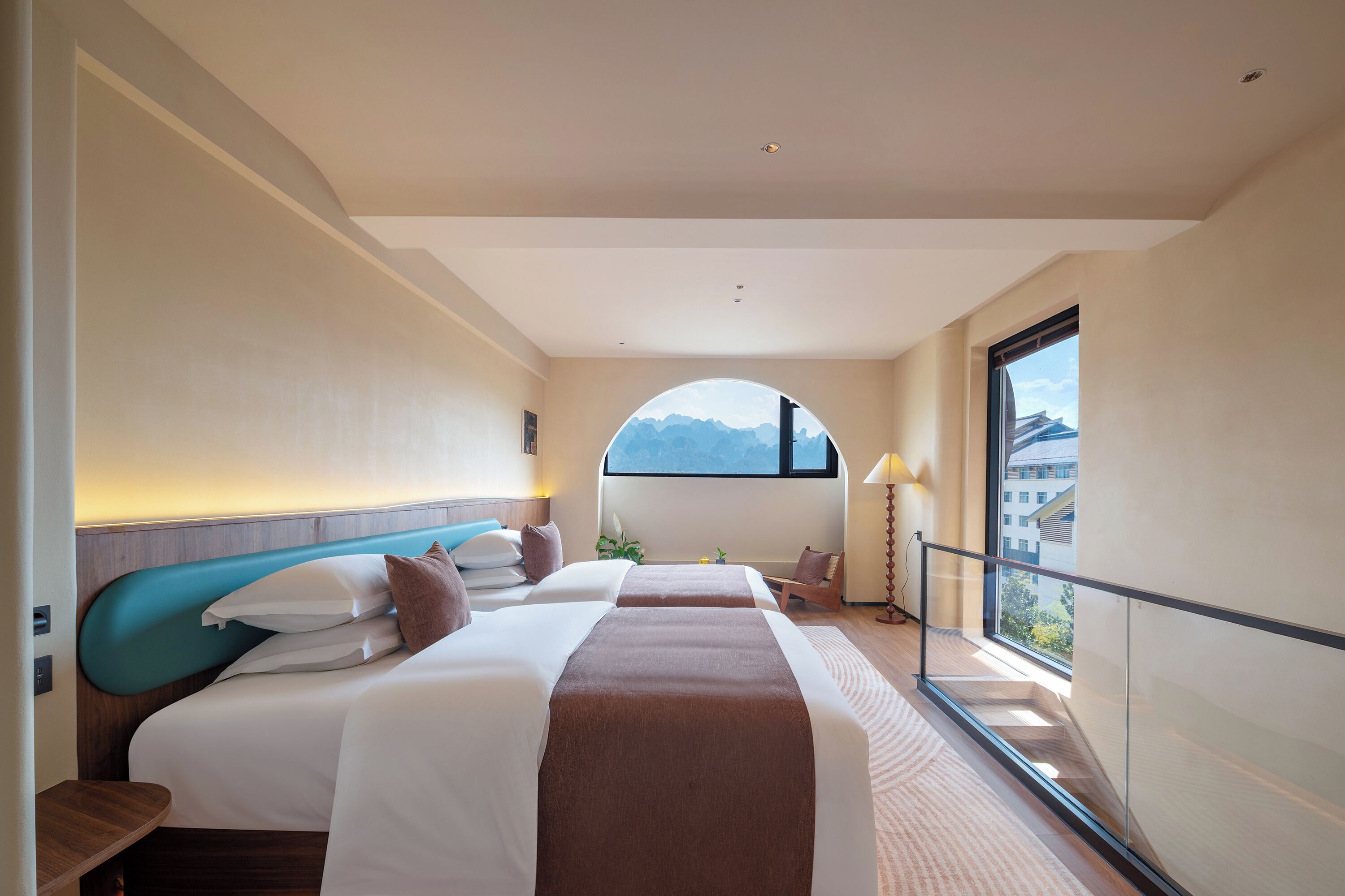 A hotel room with a large bed, a desk, a chair, and a view of the mountains through a window.