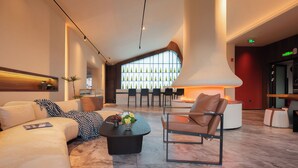 A modern lobby with a curved seating area, a large window with a geometric pattern, and a central table with a vase of flowers. - YUJIE HOTEL (Zhangjiajie)