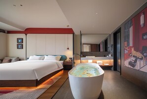 A modern hotel room with a large bed, a bathtub, a desk, and a bathroom.