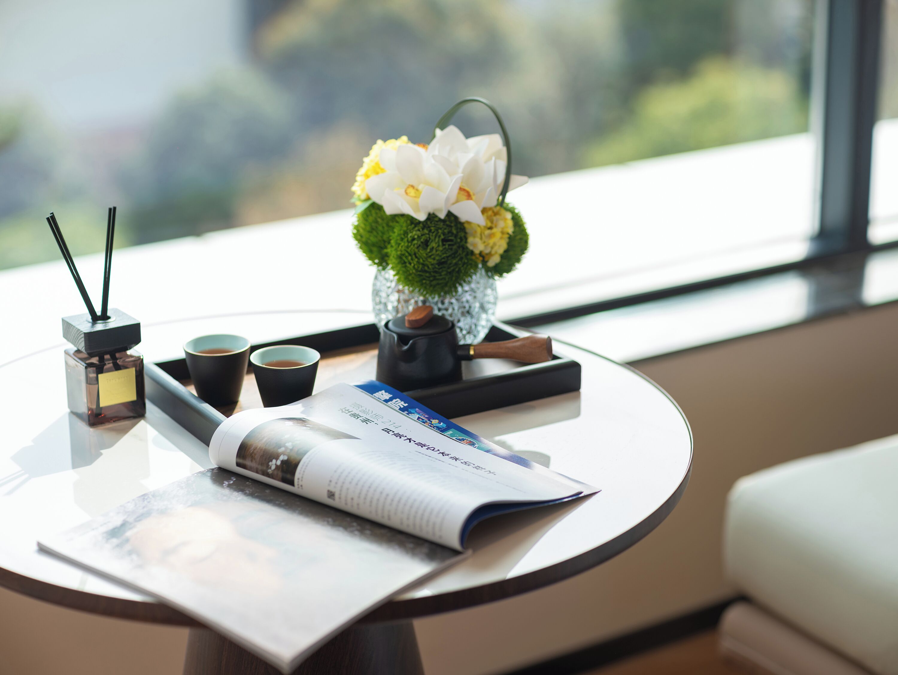 Una mesa con una revista, dos tazas, una botella y un florero con flores.