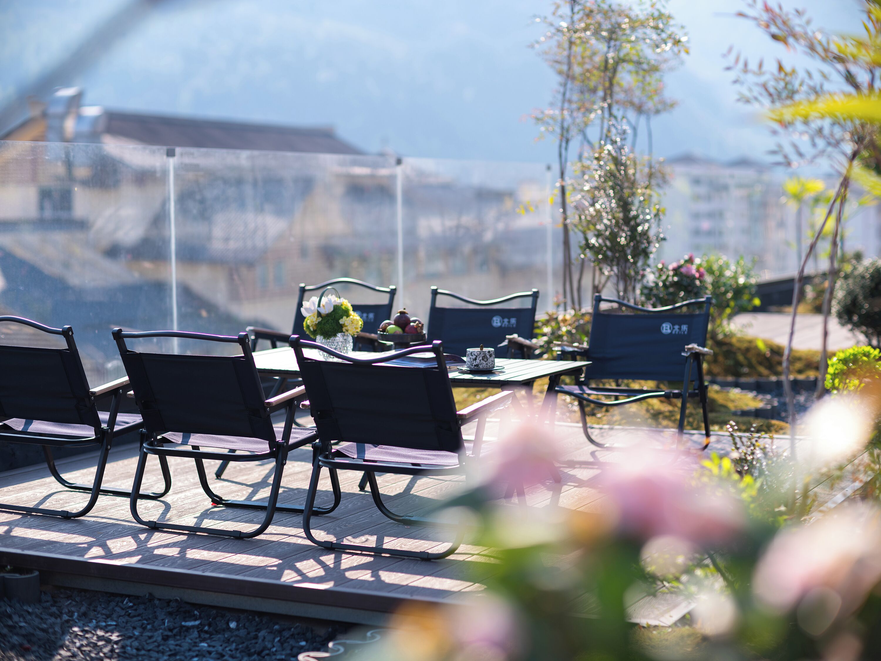 Outdoor seating with tables and chairs, a vase with flowers, and a view of buildings in the background.
