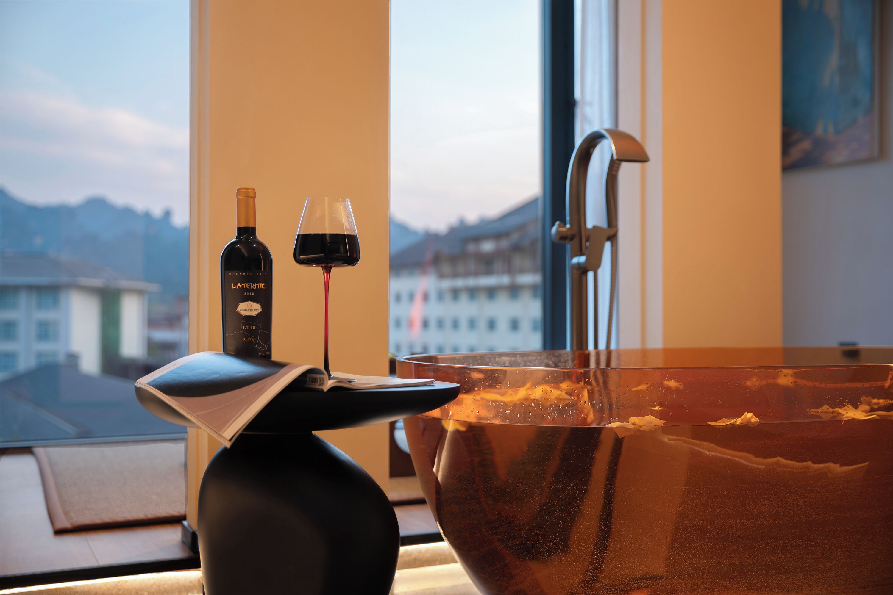 A modern bathroom with a large bathtub, a wine bottle, and glasses on a tray.