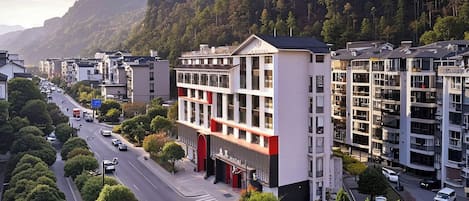 A multi-story hotel with a modern facade, located in a mountainous area with a road in front.