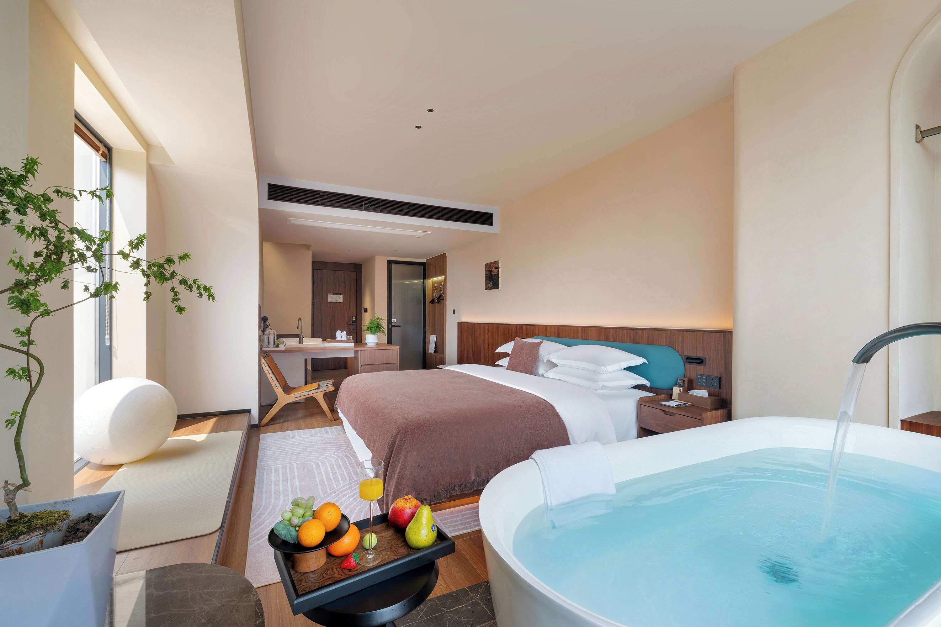 Una habitación de hotel moderna con una cama grande, un baño independiente con bañera, un comedor y un pequeño balcón.