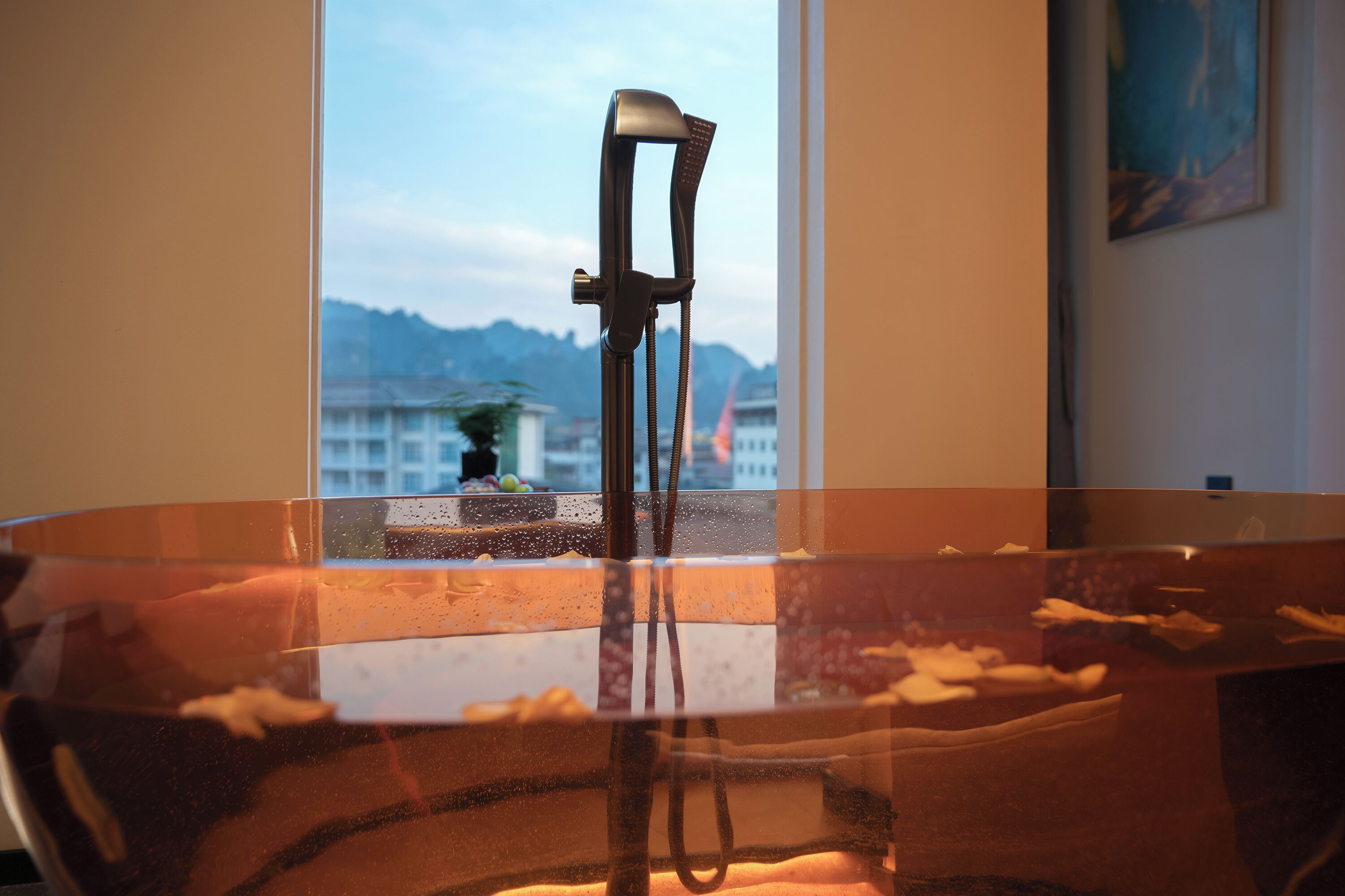 Une salle de bain dotée d’une douche à parois de verre, d’une fenêtre offrant une vue dégagée sur les bâtiments et les montagnes, et d’un porte-serviettes.