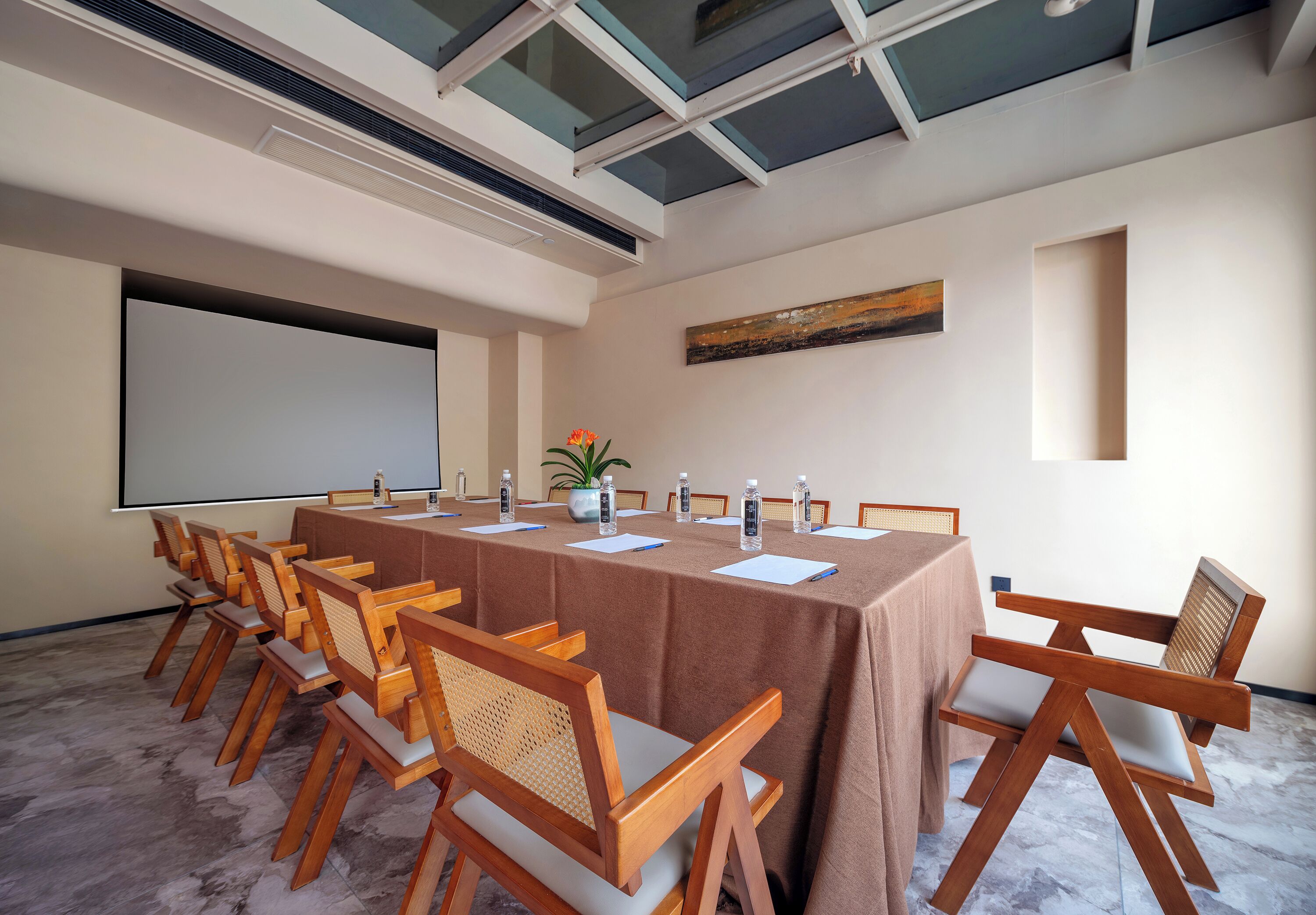 Une salle de conférence avec une longue table, des chaises en bois, un écran de projection et un tableau au mur.