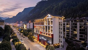 A hotel with a modern design, located at a street corner with a view of mountains. - YUJIE HOTEL (Zhangjiajie)