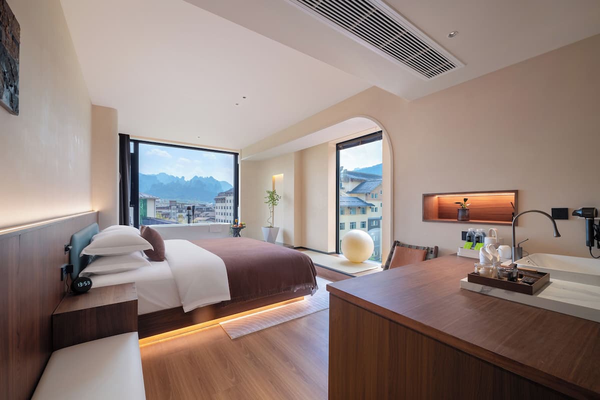 A modern hotel room with a bed, bedside table, and a desk with a sink.