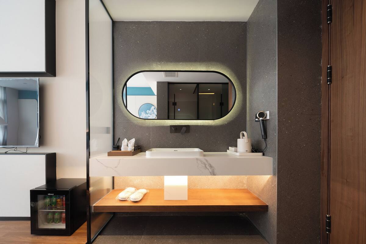 A modern bathroom with a large mirror, a sink, and a bench.