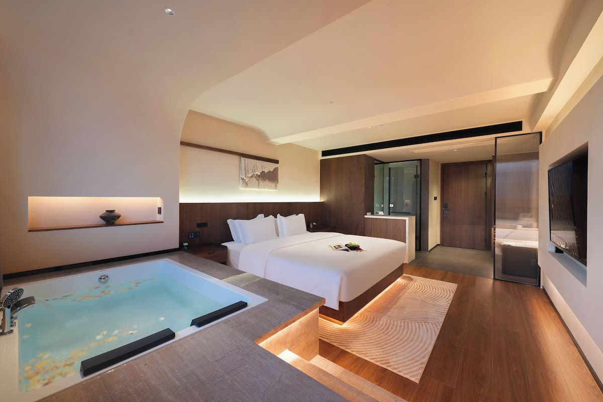 A modern hotel room with a large bed, a separate bathtub, a flat-screen TV, and a walk-in closet.