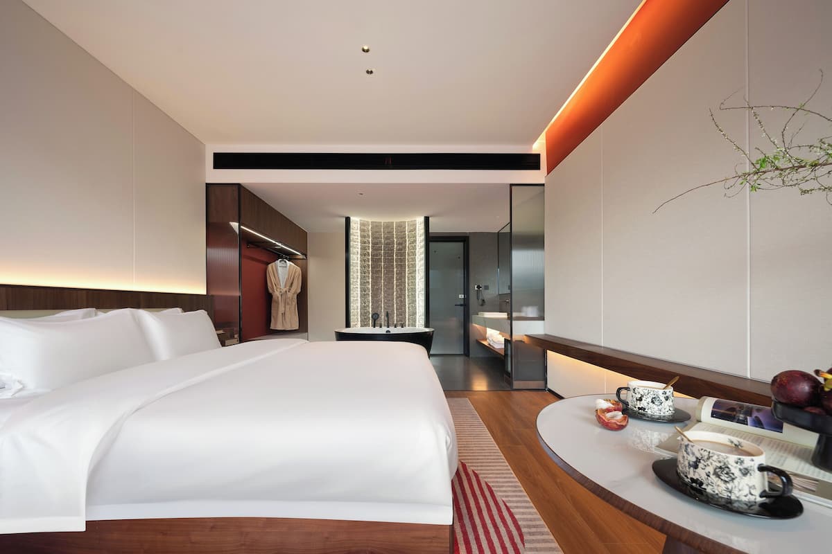 A modern hotel room with a large bed, a vanity with a mirror, and a small table with cups and a book.