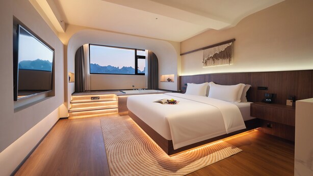A modern hotel room with a large bed, a TV, a bathroom, and a view of the mountains. - YUJIE HOTEL (Zhangjiajie)
