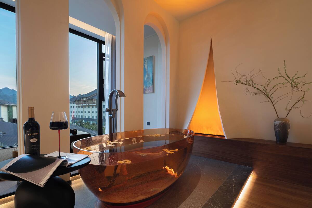 A modern bathroom with a large copper bathtub, a wine bottle, and a glass of red wine on a table.