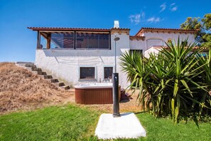 A modern two-story house with a hot tub, a staircase leading to the upper level, and a garden with a palm tree.