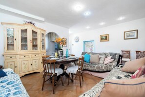 A dining area with a wooden table, chairs, a cabinet with glass doors, a sofa, and a wall clock.
