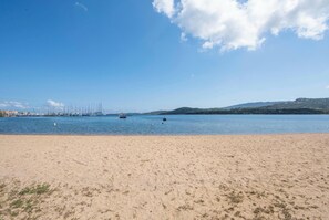 A sandy beach with calm water, boats, and distant hills.