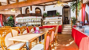 A restaurant with wooden tables and chairs, a bar area with stacked plates, and a kitchen visible in the background. - Salamandra 11 Apartamenty Góralskie (Koscielisko)