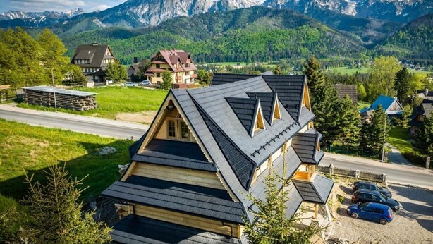 A mountain village with traditional houses, a road, and a view of snow-capped peaks. - Salamandra 11 Apartamenty Góralskie (Koscielisko)