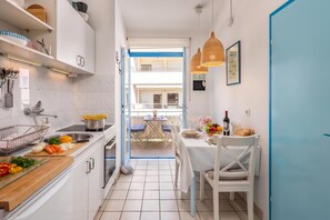Een smalle keuken met witte kastjes, een spoelbak en een eethoek met een tafel gedekt voor twee personen.