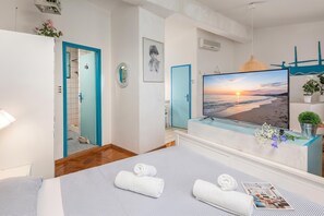 A hotel room with a bed, a TV, a bathroom, and a view of the beach.
