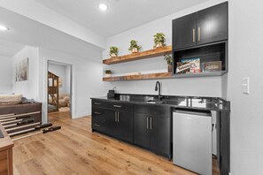 A modern kitchen with black cabinets, wooden shelves, and a built-in dishwasher.