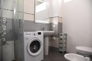 A modern bathroom with a washing machine, sink, toilet, and a glass shower enclosure.