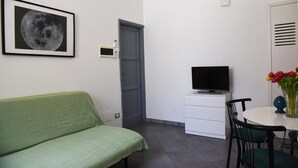 A room with a green sofa, a television on a white cabinet, a dining table with chairs, and a door. - Apartment 'Viabalduini2' with Wi-Fi and Air Conditioning (Lecce)