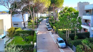 Une rue résidentielle bordée de voitures garées et d’arbres, qui mène à un immeuble moderne doté de balcons.