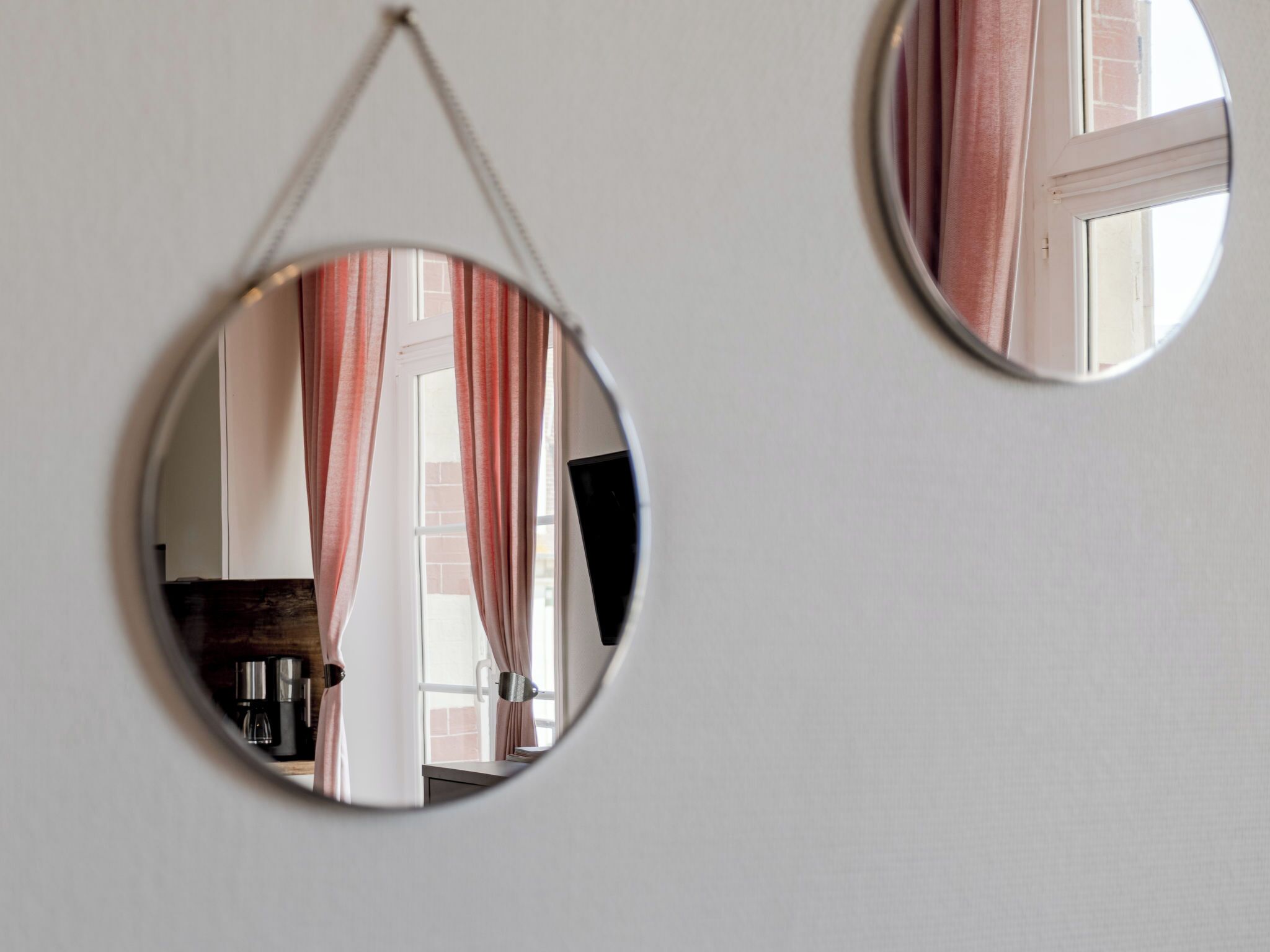 Deux miroirs ronds sont fixés au mur et reflètent une fenêtre avec des rideaux ainsi qu’une machine à café.