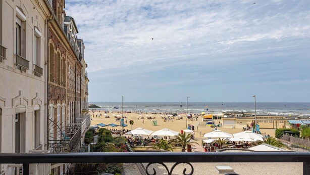 Vista desde un balcón con barandilla, que da a una playa de arena con sombrillas y gente.