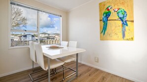 Un coin repas avec une table blanche, des chaises et une fenêtre donnant sur des maisons.
