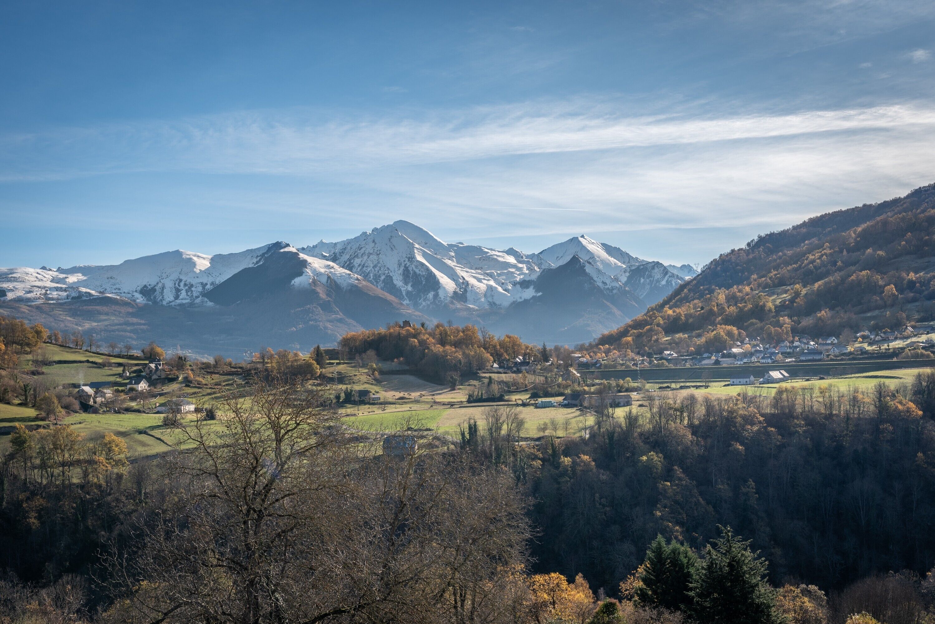 Eine gebirgige Landschaft mit schneebedeckten Gipfeln, einem Tal mit verstreuten Häusern und dichten Wäldern.