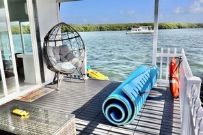 Ein Bootsdeck mit einem gepolsterten Stuhl, einer zusammengerollten Matte, einer Rettungsboje und einem kleinen Boot im Hintergrund.