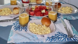 Et spisebord med morgenmadsprodukter, udsigt til havet og et hvidt gelænder.