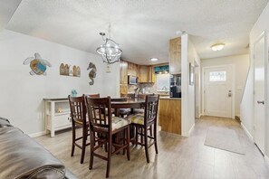 Een kleine keuken met houten kastjes, een eettafel met stoelen en een kroonluchter.