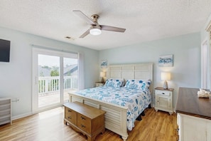 A bedroom with a bed, bedside tables, a ceiling fan, a window, and a balcony.