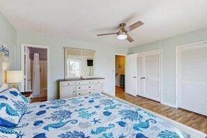 Ein Schlafzimmer mit Bett, Deckenventilator, Kommode, begehbarem Kleiderschrank und Bad.